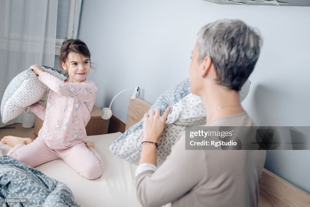 Little girl playing a pillow fight with mom in the evening