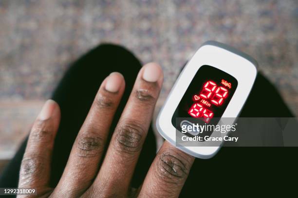 woman checks her oxygen saturation level and heart rate - puls oxymeter stock-fotos und bilder