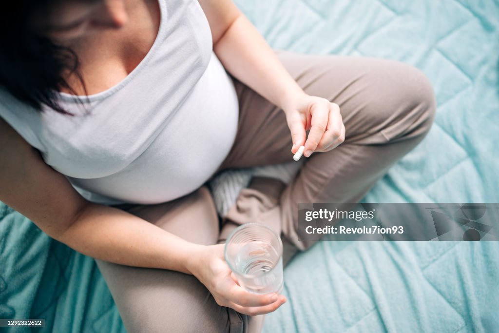 Pregnant woman taking pill at home