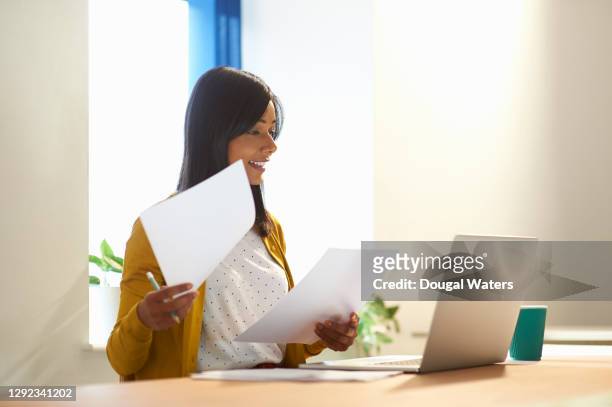 asian woman sitting at desk with laptop and paperwork. - sri lankan ethnicity stock pictures, royalty-free photos & images