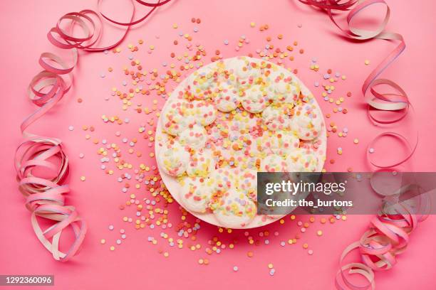 high angle view of cream cake with colourful sugar sprinkles and paper streamers on pink background - cream cake stock pictures, royalty-free photos & images