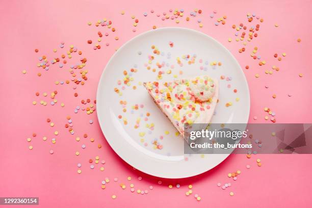 high angle view of piece of cream cake with colourful sugar sprinkles on a plate on pink background - sprinkles stock-fotos und bilder