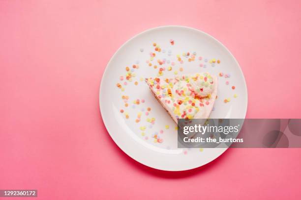 high angle view of piece of cream cake with colourful sugar sprinkles on a plate on pink background - slice of cake stock pictures, royalty-free photos & images