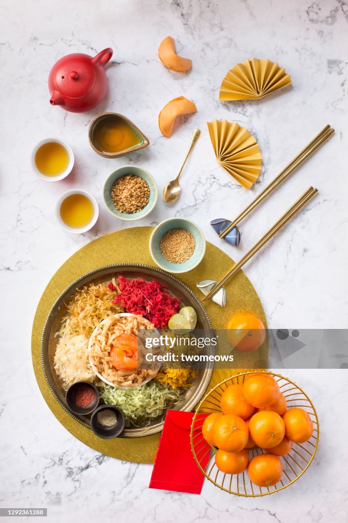 Chinese new year food, raw fish salad “Yusheng” and other traditional food and drinks on marble table top flat lay image.