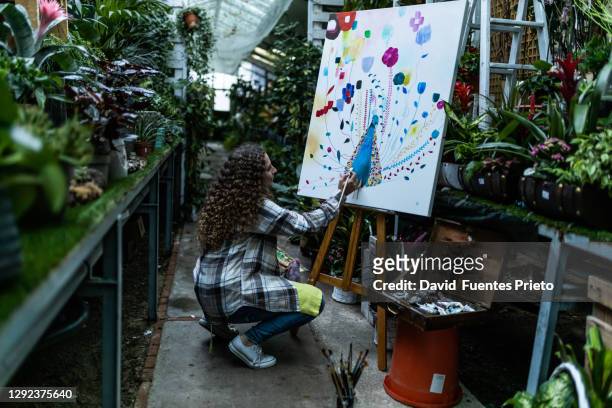 woman painter painting a picture in an indoor garden - art easel stock-fotos und bilder