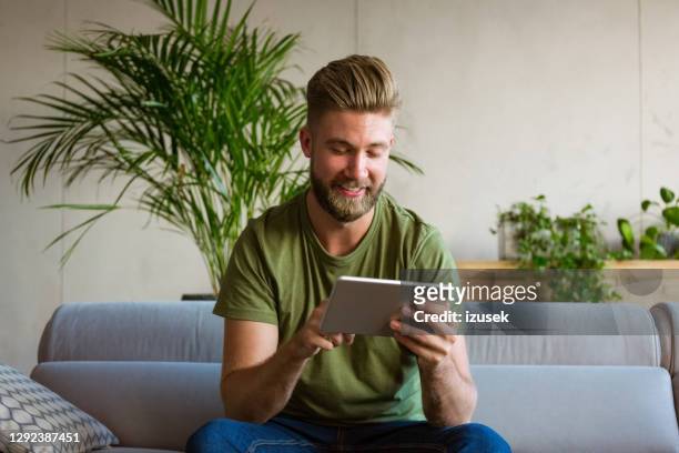 young man using digital tablet at home - green sofa stock pictures, royalty-free photos & images