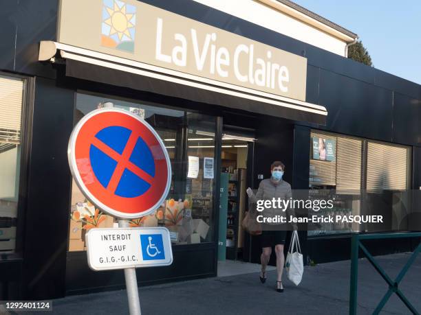 Une femme avec un masque chirurgical sort avec un sac de courses du magasin "La Vie Claire", 26 mars 2020, La-Frette-sur-Seine, France