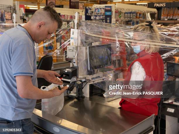 Caissière avec un masque, protégée derrière un film plastique et client portant un masque dans un magasin de distribution alimentaire "U" le 27 avril...