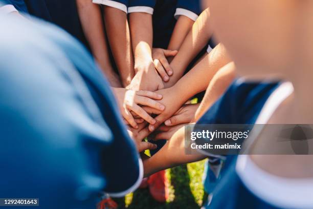 Group of happy children in sports team stacking hands outdoor in a summer day. Children team sports. Boys at sports camp stacking hands before a game. School age children in a team at the grass field