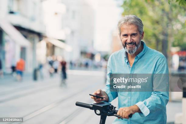 mature man renting an e-scooter, using his smart phone - 50 59 years stock pictures, royalty-free photos & images