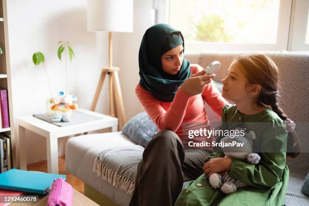 muslim mother measuring the daughter's temperature during covid-19 - temperature checkpoint stock pictures, royalty-free photos & images