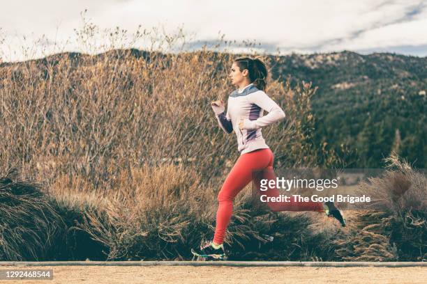 side view of female athlete running by field - running stock pictures, royalty-free photos & images