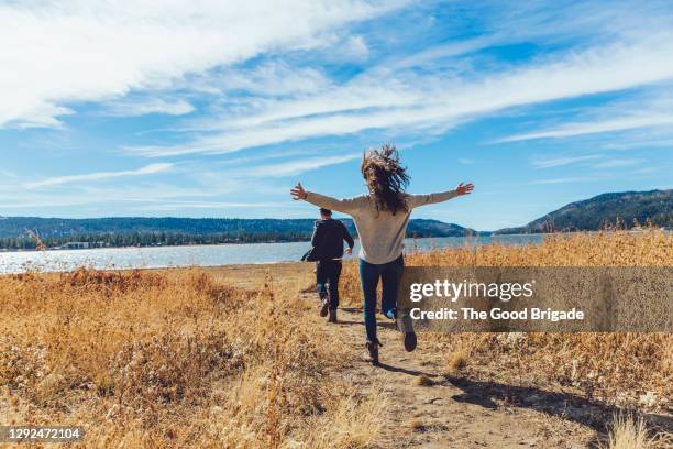 full length rear view of couple running on dirt path by lake - weekend activiteiten stockfoto's en -beelden
