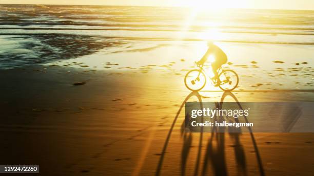 man casting long shadow cycling on oregon beach - drone shot - netarts bay stock pictures, royalty-free photos & images