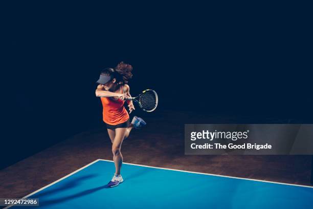 female tennis player practicing on court against black background - blue tennis court stock pictures, royalty-free photos & images