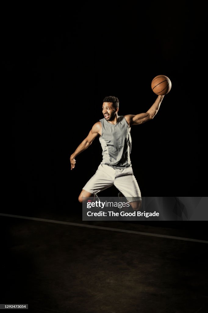 Confident male player jumping with basketball against black background