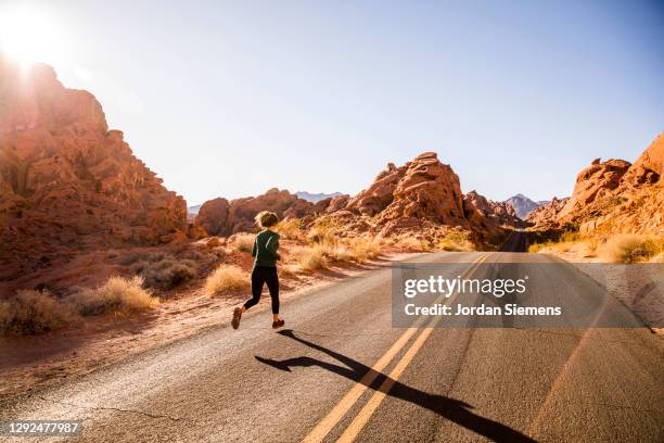 a woman running down a scenic road leading through the desert. - nevada nature stock pictures, royalty-free photos & images