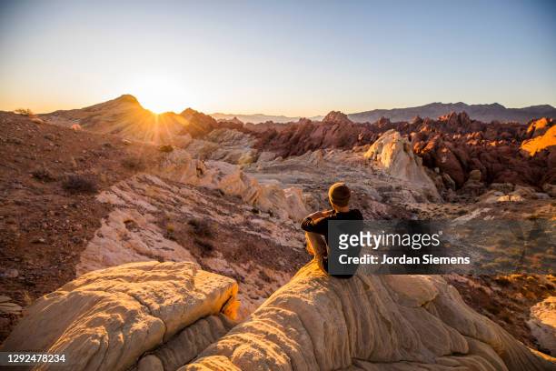 a man sitting on a rock watching the sunrise in the desert. - outdoor guy sitting on a rock stockfoto's en -beelden