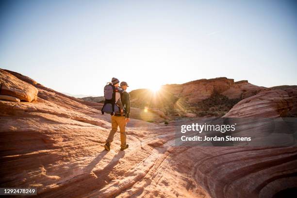 a man carrying his son in a backpack while hiking in the red rocky desert landscape. - paysage fun photos et images de collection