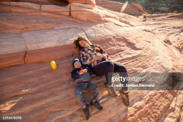 a mother and her son taking a rest while hiking on the red rocky terrain of the south west desert. - nevada stock-fotos und bilder