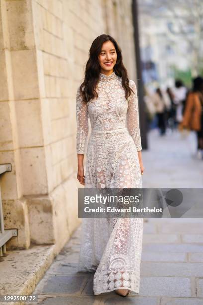 Guest wears Dior earrings, a high neck white lace see-through mesh full-length dress with floral embroidery, outside Dior, during Paris Fashion Week...