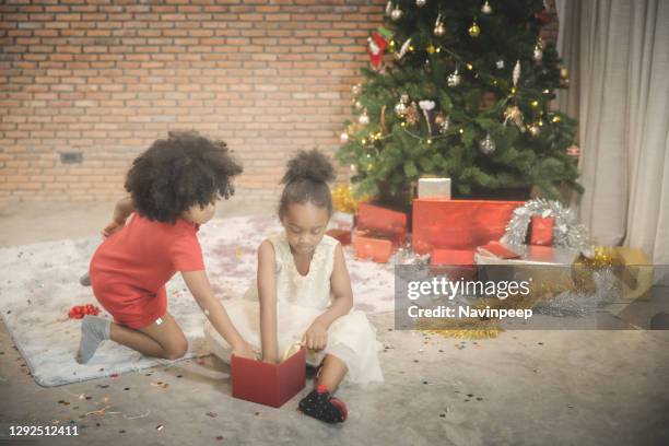 african american children playing around christmas tree, opening present - the red room opening party inside stock pictures, royalty-free photos & images