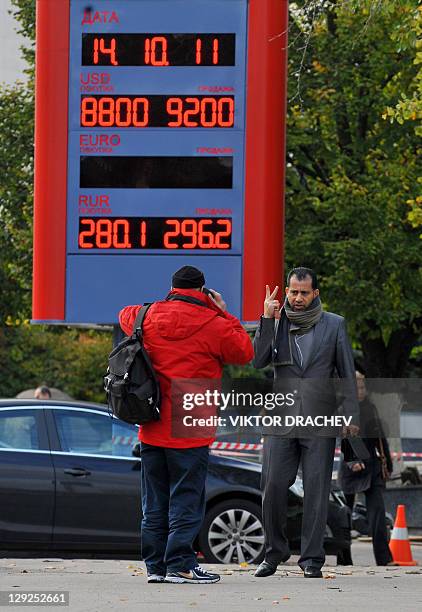 People stand near a board listing foreign currency rates against the Belarus' ruble outside an exchange office in Minsk on October 14, 2011. Belarus...