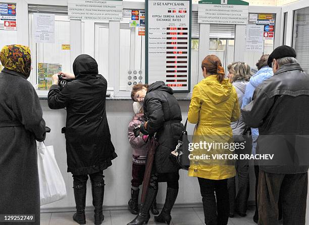 People stand in queue near a board listing foreign currency rates against the Belarus ruble inside an exchange office in Minsk on October 14, 2011....