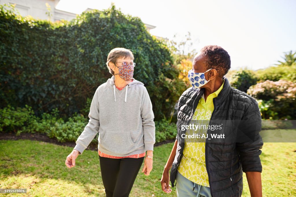 Two senior women in face masks walking in a park