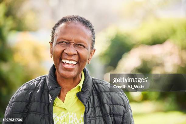senior woman laughing while standing in a park - baby boomer stock pictures, royalty-free photos & images