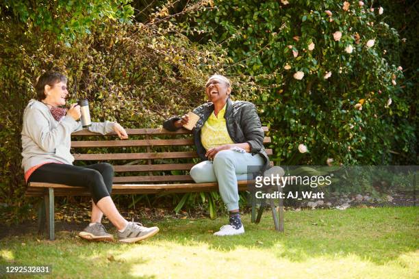 laughing senior friends sitting together on a park bench - social distancing stock pictures, royalty-free photos & images