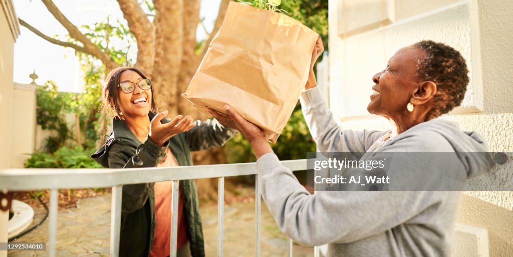 Mujer sonriente entregando una bolsa de comestibles a un anciano en casa