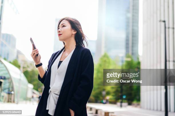 portrait of confident young business woman with smartphone - japanese bussiness woman looking up stock-fotos und bilder