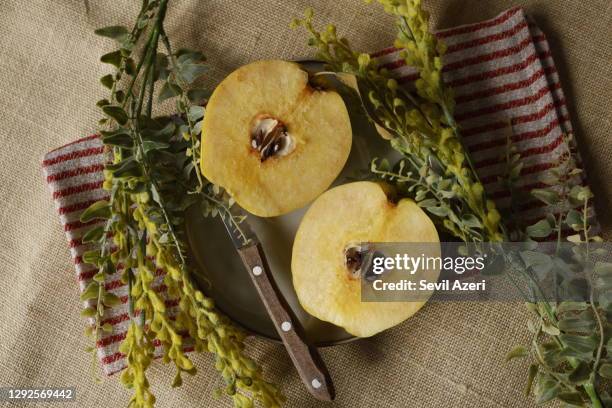 two slices of quince on a plate on a red beige striped napkin and burlap background, yellow wildflowers around it - quince stock pictures, royalty-free photos & images