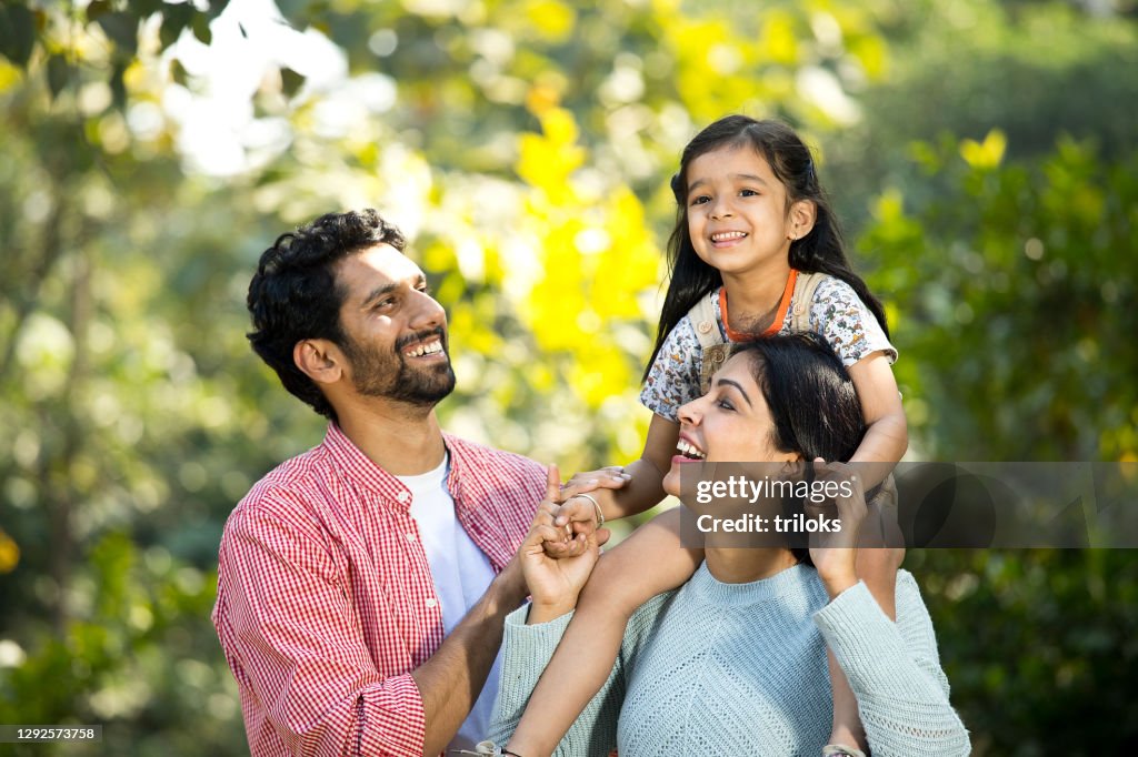 Happy mother with father carrying their daughter on shoulder at park