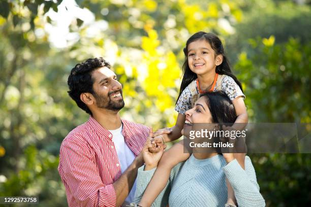 happy mother with father carrying their daughter on shoulder at park - family stock pictures, royalty-free photos & images