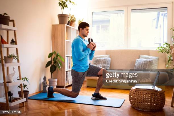 young man working out split squats with kettlebell, online workout on laptop - home workout stock pictures, royalty-free photos & images