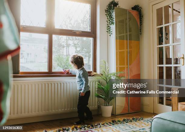 little girl with a small toy playing by a sunny window in a domestic room - calor fotografías e imágenes de stock