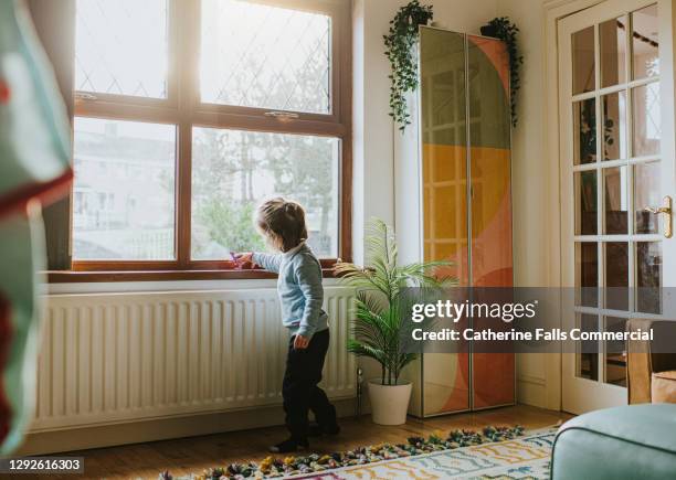 little girl with a small toy playing by a sunny window in a domestic room - radiator stock pictures, royalty-free photos & images