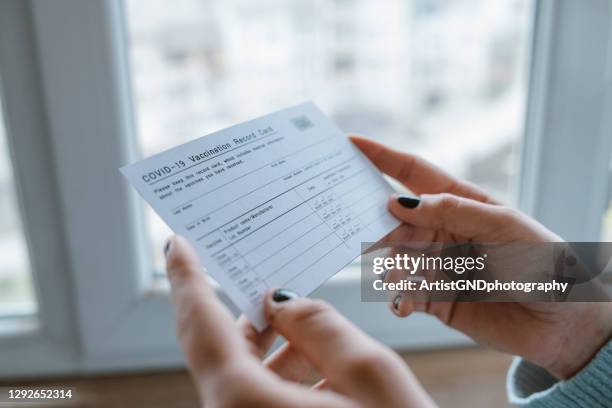 woman holding covid-19 vaccination record card. - travel vaccination stock pictures, royalty-free photos & images