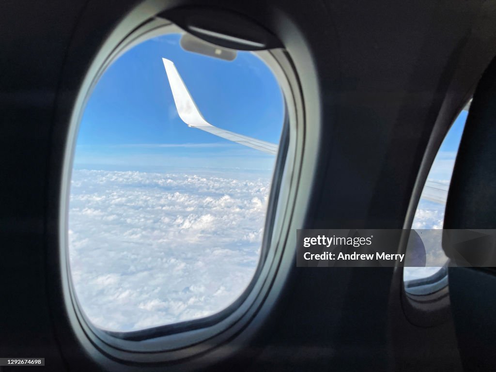 Airplane window, view of aircraft wing, blue sky and clouds