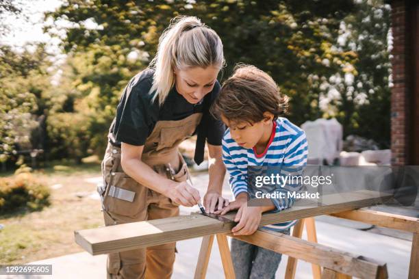 mother measuring wooden plank by son at construction site - front or back yard - fotografias e filmes do acervo