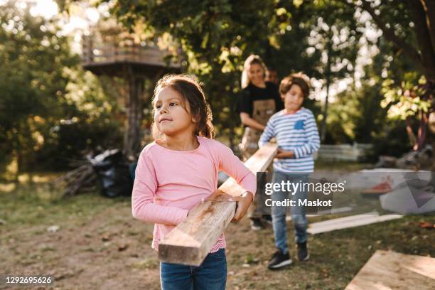 confident girl with family carrying wooden plank in yard - blue collar family stock pictures, royalty-free photos & images