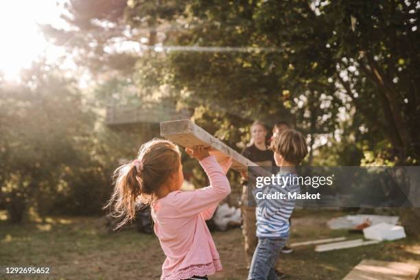 parents and children carrying wooden plank in yard - bauen holz stock-fotos und bilder