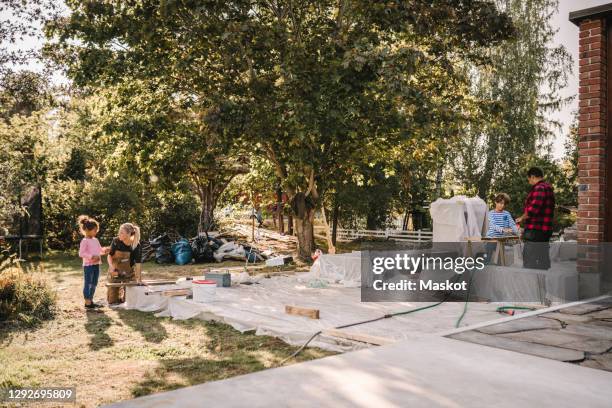 daughter talking to mother while son learning carpentry from father in yard - backyard renovation stock pictures, royalty-free photos & images