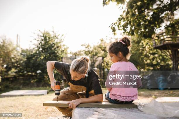 daughter looking at mother using drill machine on wooden plank in backyard - plank meubels photos et images de collection