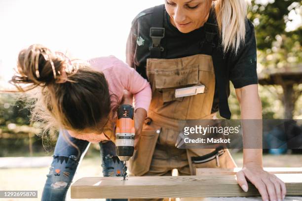 daughter using drill machine on wooden plank by mother in yard - kids instruments fotografías e imágenes de stock