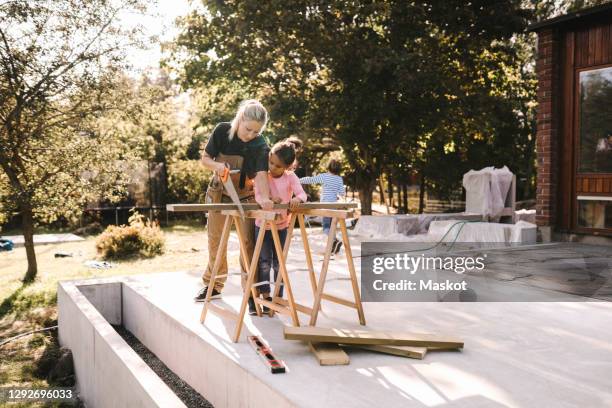 mother cutting wood with hand saw by daughter outside house - sawing stock pictures, royalty-free photos & images