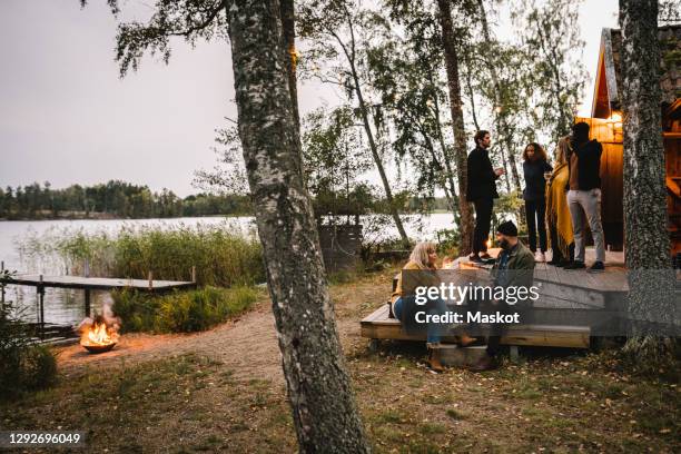 male and female talking while friends standing outside cottage during social gathering - stockholm beach stock pictures, royalty-free photos & images