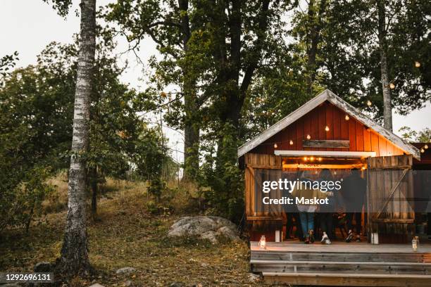 rear view of male and female friends entering cottage during social gathering - huisje stockfoto's en -beelden